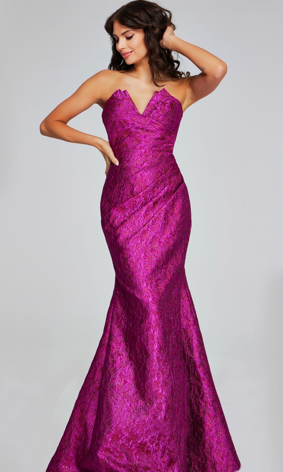 A woman models the Jovani 39114, a strapless brocade formal dress with a floor-length mermaid silhouette in shiny magenta fabric, posed against a plain background.